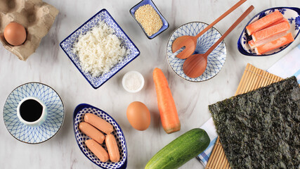 Fototapeta na wymiar Top View Kimbap/Gimbap Ingredients/Korean Rice Roll on White Marble Table. Laver/Nori, Carrot, Rice, Salt, Sesame Seed, Cucumber, Crabstick, and Sausage.
