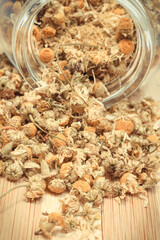Dried chamomile pouring out of glass jar. Alternative medicine