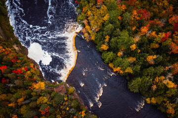 Incredible look down aerial photograph of the upper waterfall cascade at Tahquamenon Falls with beautiful autumn foliage on the trees with green, yellow, red and orange leaves surrounding the river.