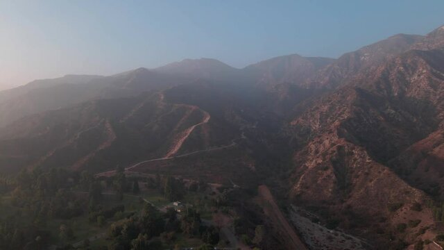 Aerial drone shot push back of Sylmar mountains, park and houses during sunset in San Fernando Valley, California.