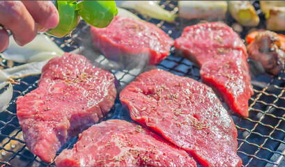 屋外のオープングリルで牛肉を網焼きしている様子