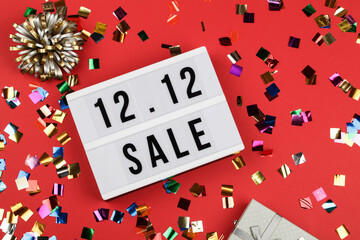 12.12 sale text on white lightbox, holiday ribbon and box around on red background.