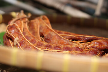 Wet and sticky Tamarind or Tamarindus indica,after peeled,fruit stalk still included,on  Banana leaves on a basket.