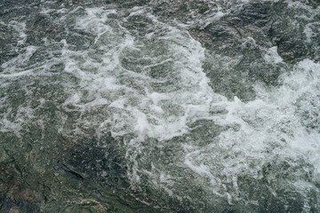 Full frame nature background of water riffle of mountain river. Powerful water stream of mountain creek with rapids. Natural textured backdrop of fast flow of mountain brook. Rapids texture close-up.