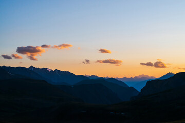 Colorful dawn landscape with beautiful mountains silhouettes and golden blue gradient sky with clouds. Vivid mountain scenery with picturesque multicolor sunset. Scenic sunrise view to mountain range.