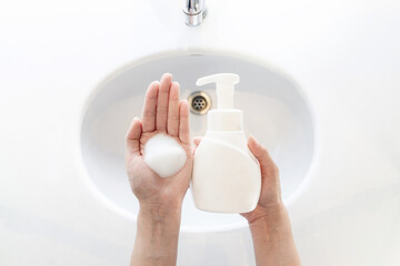 Hand holding foaming soap pump bottle and White bubbles foam soap in hands women.