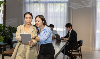 Two business female workers in formal uniform using handheld technology or digital device to check for daily plan. Lifestyle technology is in hands of young entrepreneur ladies