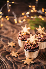 Fototapeta na wymiar Chocolate cupcakes with star shaped cookies on a wooden background. Christmas mood. Sweets for any occasion. In the background are yellow lights from the garland