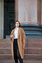 Fashionable young beautiful stylish woman in brown coat walking on street. Autumn fashion trend for smiling, happy, purposeful female. Concept style, fashion, beauty and achievement goals. Copy space