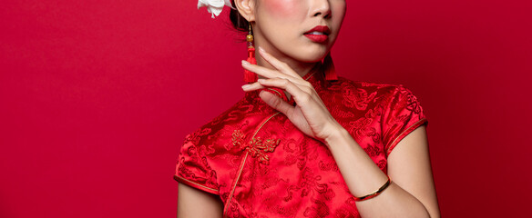 Asian woman in traditonal Chinese Cheongsam dress touching her face in isolated red banner background - obrazy, fototapety, plakaty