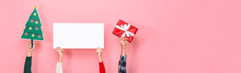 Hands holding gift box, Christmas tree and white paper board with blank space for text in pink isolated banner background