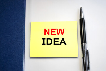 A new idea is written on a piece of paper that is located on a light background among a blue Notepad and pen.