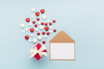 Valentine's Day holiday card. Red white small shiny hearts, gift box and empty card with envelope on pastel blue background.