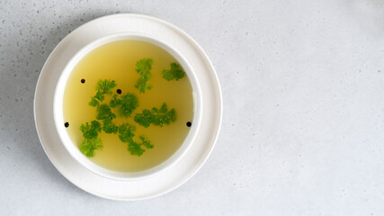 Homemade beef bone broth in white bowl with parsley leaves and peppercorns. Health benefits. Collagen is good for joints. Flat lay. Copy space.