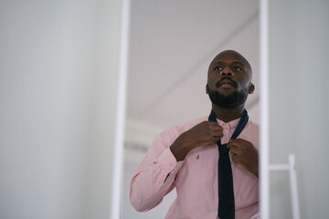 African American man in shirt dressing up and adjusting tie on neck at home.