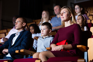 Young parents visiting theater with their tween son, consumed with watching theatrical performance