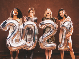 Beautiful Women Celebrating New Year.Happy Gorgeous Female In Stylish Sexy Party Dresses Holding Silver 2021 Balloons, Having Fun At New Year's Eve Party. Holiday Celebration.Charming Models 