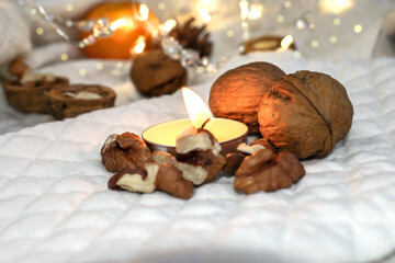Burning candle among walnuts on a white background with lights and bokeh.