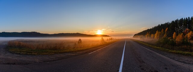 Sunrise, in the foreground the road passing through the field is covered with a thin layer of fog