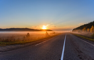 Fototapeta na wymiar Sunrise, in the foreground the road passing through the field is covered with a thin layer of fog