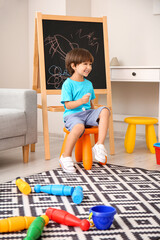 Happy little boy near painted blackboard in kindergarten