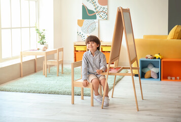 Cute little boy near easel in kindergarten