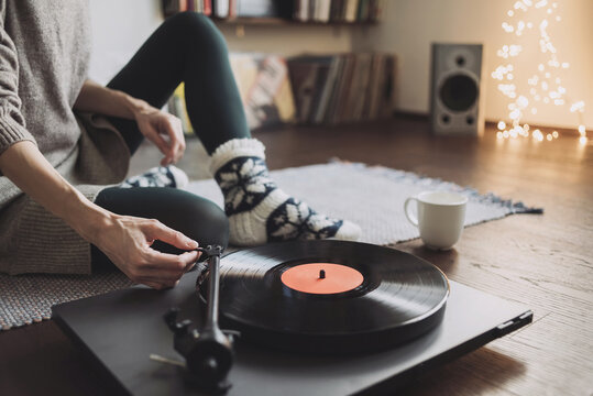 Young woman listening to music, relaxing, enjoying life at home. Girl wearing warm winter clothes having fun. Turntable playing vinyl LP record. Leisure, music, hobby, lockdown, lyfestyle concept