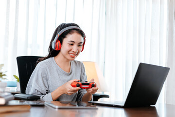 Funny Young woman wearing earphones playing computer game on laptop with joypad.