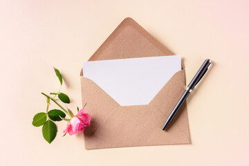 Invitation or greeting card mockup in a brown craft envelope, shot from above on a pink pastel background with a flower