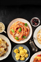 Italian pastas, spaghetti and ravioli, overhead flat lay shot on a black background, with olives and a place for text