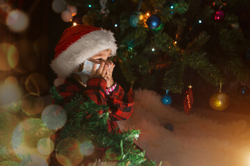 coronavirus, cavid-19 in the new year. a little girl in a red Santa Hat and mask is sitting under the Christmas tree at home.