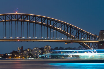 A boat passing through Sydney Harbour Bridge at night.