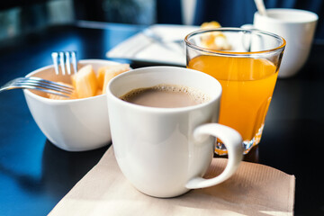Continental breakfast with cup of coffee, glass of orange juice and sliced melon in bowl on table