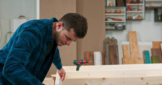 Middle - aged carpenters build a solid wood wall in a carpentry workshop. The carpenter and his apprentice measure the construction of the wooden frame of the wall.