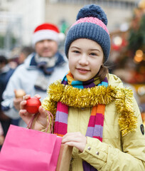 Portrait of smiling teen girl with father holding shopping bags with purchases on street Christmas market