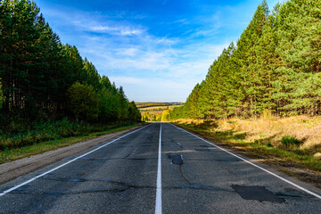 The old asphalt road goes into the distance to the autumn forest