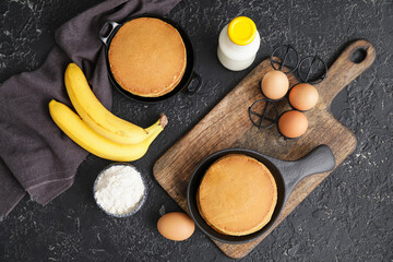 Tasty banana pancakes with ingredients on dark background