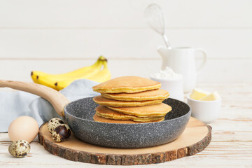 Frying pan with tasty banana pancakes on table