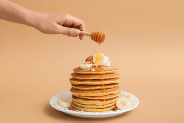 Woman pouring honey onto tasty banana pancakes on plate against color background