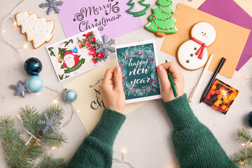 Woman writing greeting postcards for Christmas and New Year celebration at table