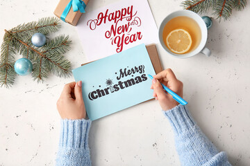 Woman writing greeting postcard for Christmas celebration at table