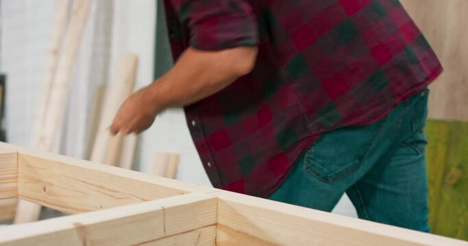 Concentrated young bearded passionate carpenter drives a carpentry screw into a construction beam with a screwdriver in a carpentry workshop.