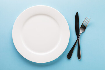 White ceramic plate and cutlery on a blue background, top view. Food background