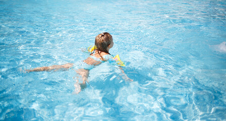 little girl swims in the pool in the outdoor water park