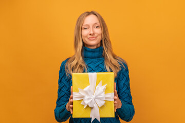 Portrait of a happy young woman holding gift decorated with ribbon. Studio shot, yellow background