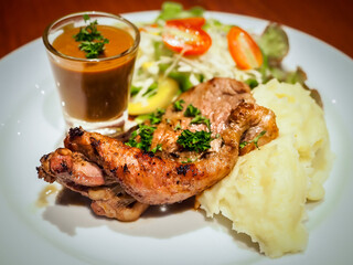 Grilled beef steak sirloin with gravy sauce in small glass, mashed potatoes and vegetable salad on white dish.