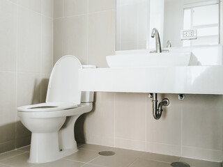 Modern stainless steel faucet on bathroom sink near the mirror on the wall and flush toilet on the corner of clean bathroom.