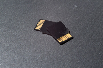 two micro sd cards lie on top of each other on a dark textured background, with golden contacts at...