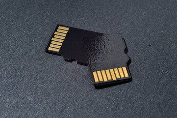 two micro sd cards lie on top of each other on a dark textured background, with golden contacts at...