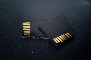 two micro sd cards lie on top of each other on a dark textured background, with golden contacts at...